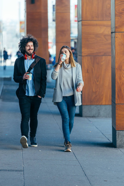 İş çifti (iş arkadaşları) kahve içerken ve birbirleriyle konuşurken fütürist modern istasyon (havaalanı) boyunca yürüyorlar. - Fotoğraf, Görsel