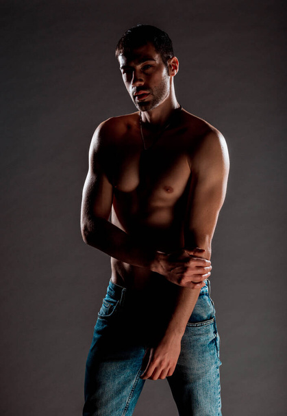 Stijlvolle mode man poseren shirtloos tegen donkere achtergrond - Foto, afbeelding
