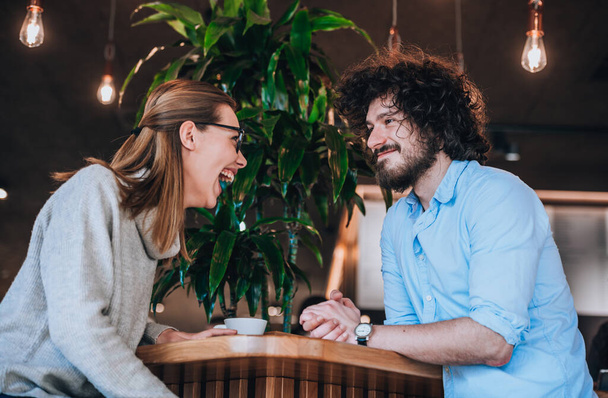 Νεαρός άντρας και γυναίκα χαμογελάνε και κάνουν μια ευχάριστη συζήτηση στο καφέ μπαρ - Φωτογραφία, εικόνα