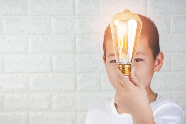 A boy wearing a white t-shirt with a light bulb in his hands on white background - 写真・画像