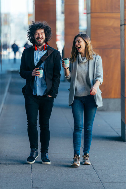 ビジネスカップル(同僚)は、コーヒーを飲みながら近代的な駅(空港)を歩いてお互いと話す. - 写真・画像