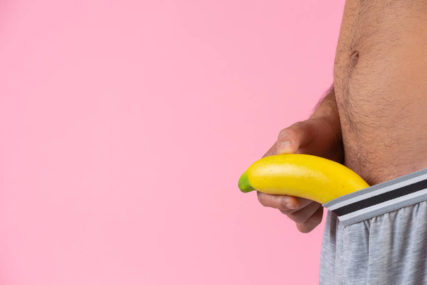 A man with a standing gesture holding a banana on the pink background - Photo, Image