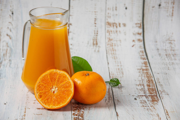 グラスの中の新鮮なオレンジジュースと白い木の花に置かれた新鮮なオレンジ - 写真・画像
