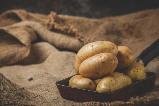 aardappelen in zwarte keramische plaat op zak - Foto, afbeelding