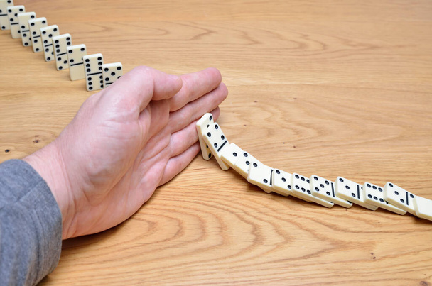 Domino αποτέλεσμα, αλυσιδωτή αντίδραση σταματά από ένα ανθρώπινο χέρι. - Φωτογραφία, εικόνα