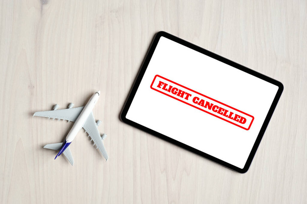 Concepto de cancelaciones de vuelos. Juguete de avión de vista superior y tableta digital con mensaje "Vuelo cancelado" en pantalla
. - Foto, imagen