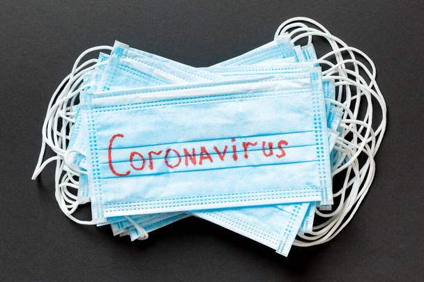 Epidemischer Hintergrund aus Coronavirus-Wort auf einem Haufen medizinischer Schutzmasken auf schwarzem Hintergrund. Weltquarantäne-Konzept. - Foto, Bild