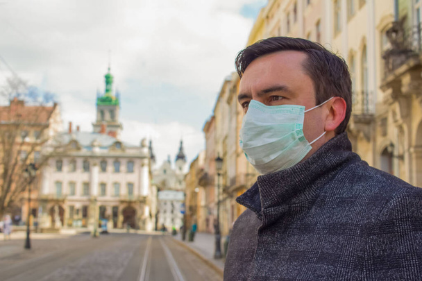 LVIV,UKRAINE, 22 March 2020: handsome young European man on the empty street wearing disposable protective face mask during pandemia of Covid-19 - Photo, Image
