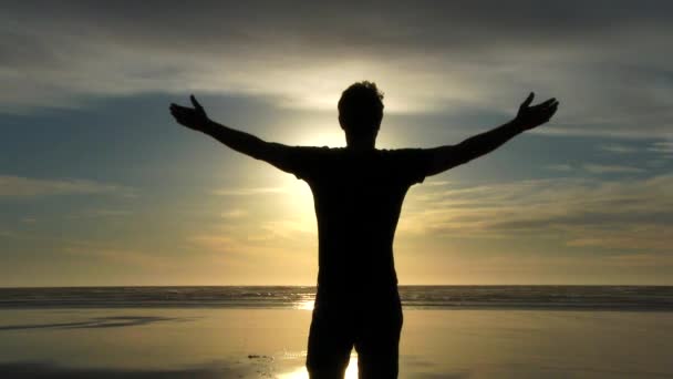 Silueta muž stojí a zvedá ruce na obloze západu slunce na pláži úplně sám těšit. - Záběry, video