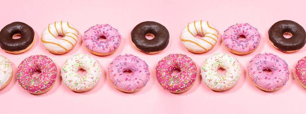 Doughnuts with multicolored glaze laid out in two rows on trendy pink background. Donuts are traditional sweet pastries. Creative web banner. - Photo, Image