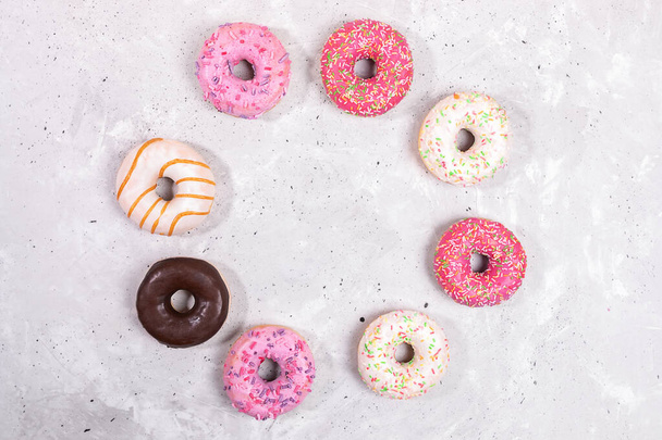 Doughnuts with multicolored glaze laid out in circle on grey concrete background. Donuts are traditional sweet pastries. Top view, flat lay, copy space in center. - Photo, Image