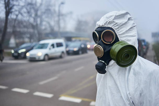 Enfoque selectivo del científico con máscara de gas y traje de protección mirando a la carretera con los coches, esperando la luz verde
. - Foto, Imagen