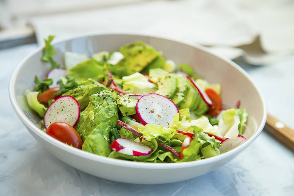 Fresh vegetable salad bowl closeup, healthy organic vegetables salad with radish, spinach, tomatoes, onion, avocado - Photo, Image