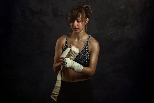 Vrouw klaar voor gevecht concept. Boxer vechter meisje in sport top, wikkelt zijn handen elastische bandages vuisten op zwart - Foto, afbeelding