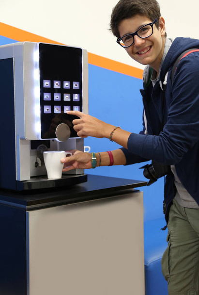 Très heureux garçon boit du café dans un distributeur de boissons chaudes
 - Photo, image