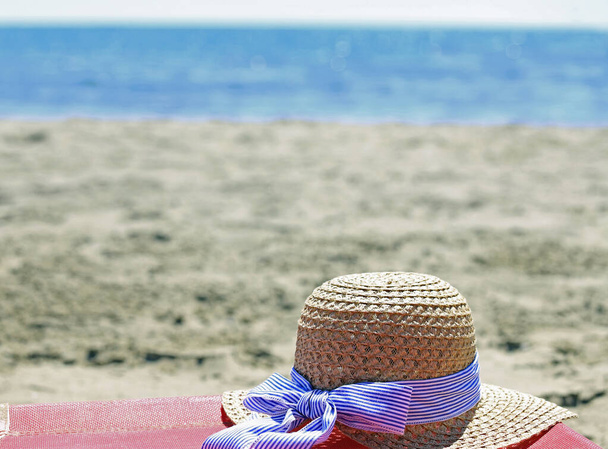 ψάθινο καπέλο πάνω από το κρεβάτι δίπλα στη θάλασσα το καλοκαίρι χωρίς ανθρώπους - Φωτογραφία, εικόνα