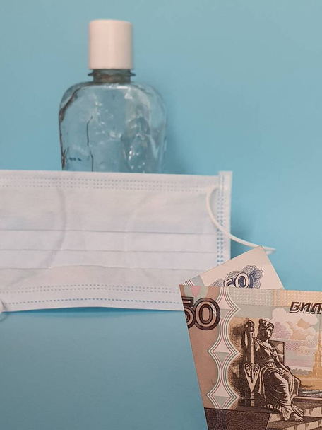 Billete ruso de cincuenta rublos, mascarilla, botella con alcohol en gel y fondo azul
 - Foto, Imagen