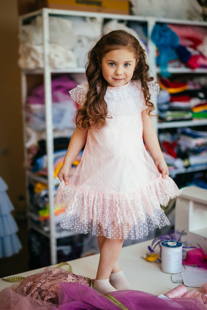 Little girl in a pink dress posing on a table in a sewing atelier - Photo, image