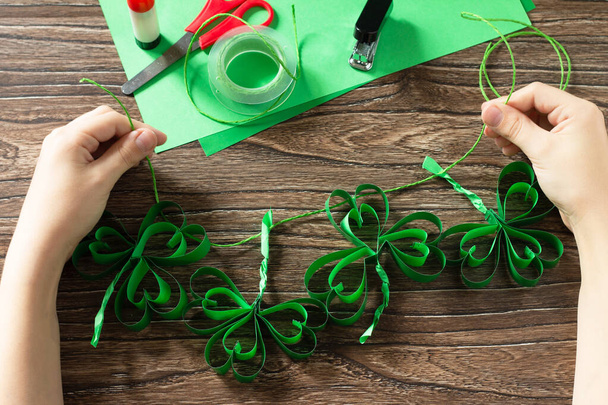 Criança detém trevo Garland St. Patrick 's Day, artesanato de papel. Feito à mão. Projeto de arte infantil, bordado, artesanato para crianças
 - Foto, Imagem