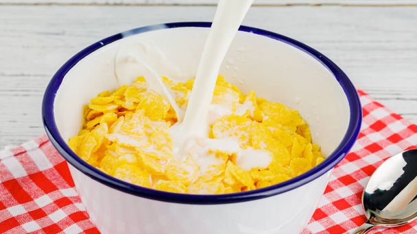 Frühstück mit Cornflakes. Milch in eine Schüssel mit Cornflakes geben. Der Joghurt spritzt in Cornflakes. Gesundes Frühstück. Lebensmittel und Getränkeindustrie. - Foto, Bild