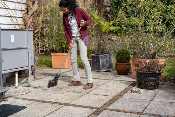 Giovane donna pulire fogliame sulla terrazza in primavera. Scena rurale nel giardino di casa
. - Foto, immagini