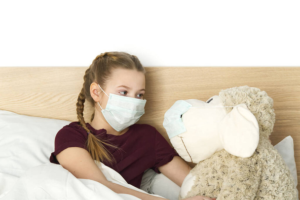 Больной грустный ребенок в маске с температурой и головной болью лежит в постели. Простуда вызывает бактерию вируса гриппа. девушка с игрушкой в спальне носить защитную маску, защитить от коронавируса концепции
. - Фото, изображение