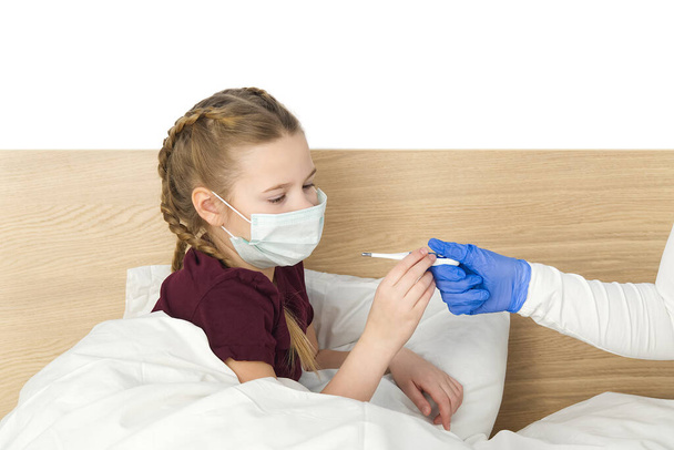 Maskeli kıza ısıyı ölçmesi ve virüsü tespit etmesi için bir termometre veriliyor. Sağlık ve hasta çocuk ve koronavirüs konsepti. - Fotoğraf, Görsel