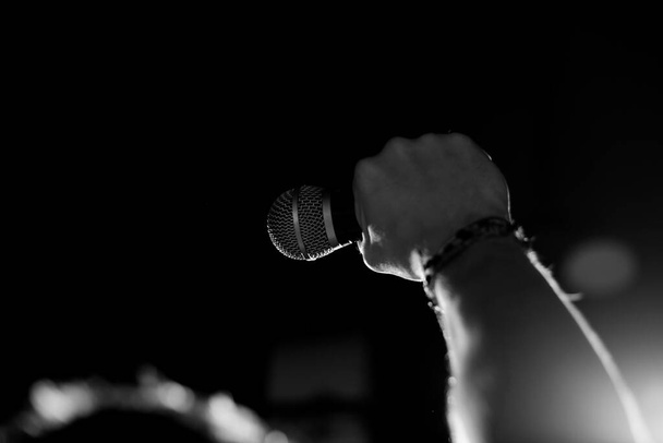 Ellerinde bileziklerle yükselen bir erkek mikrofon tutuyor. Geri ve beyaz fotoğrafçılık - Fotoğraf, Görsel