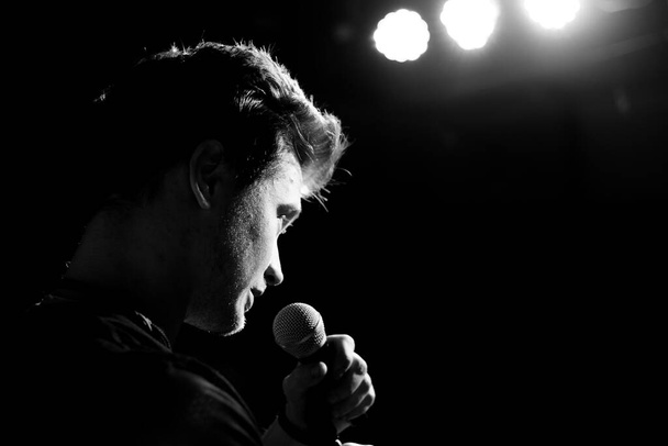 Young handsome guy emotionally sings and speaks into the microphone. Black and white photography - Foto, imagen