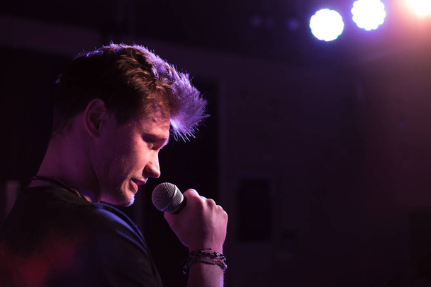 Genç yakışıklı adam duygusal olarak şarkı söylüyor ve mikrofona konuşuyor. - Fotoğraf, Görsel