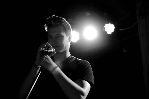 Genç yakışıklı adam duygusal olarak şarkı söylüyor ve mikrofona konuşuyor. Siyah beyaz fotoğraf. - Fotoğraf, Görsel