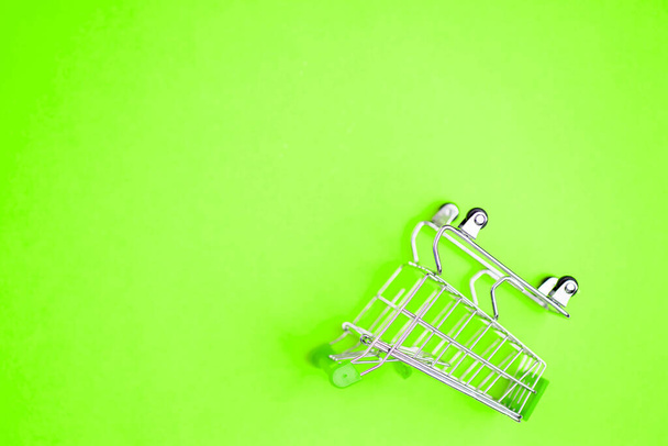 Top view, flat lay shot of shopping cart on bright green background. Copy space for text or design. Stainless steel shopping trolley upside down. Minimalist shopping concept. - Zdjęcie, obraz