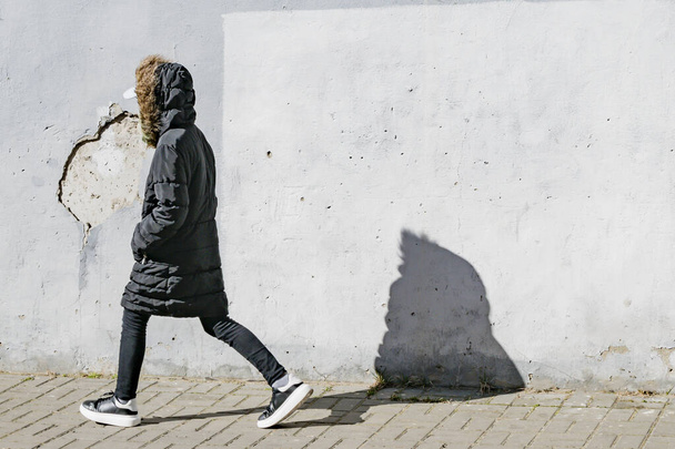 A young girl in a dark jacket walks on the street - Фото, зображення