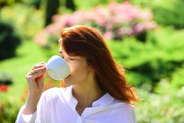 Girl drinking coffe outside, outdoor. Beautiful young woman with cup of coffee. Woman enjoys fresh coffee in the morning in spring park. - Fotoğraf, Görsel
