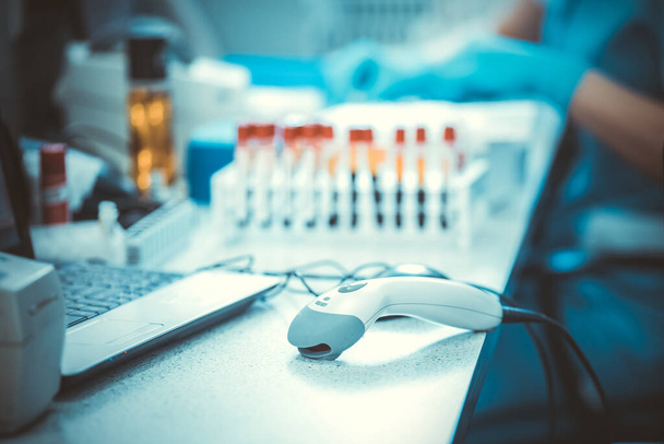 Bar codes scanner, blood sample tubes and laptop with lab technician hands on background. Coronavirus COVID-19 laboratory analysis workplace. - Φωτογραφία, εικόνα