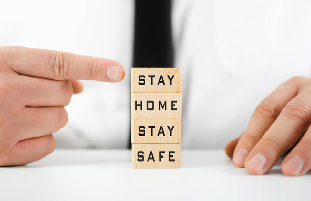 Zakenman wijst naar Stay Home, Stay Safe geschreven op houten blokken in een conceptueel beeld voor zelfquarantaine tijden tijdens virusuitbraak. - Foto, afbeelding