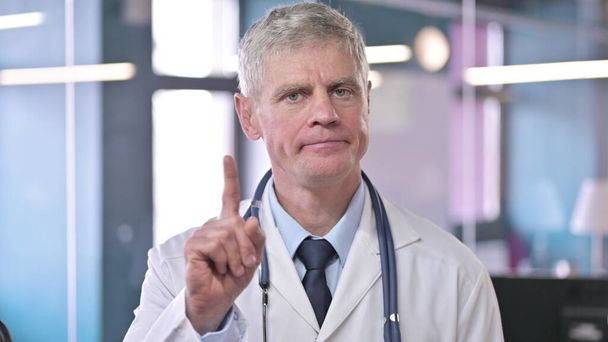 Porträt eines Arztes mittleren Alters, der mit dem Finger Nein sagt - Foto, Bild