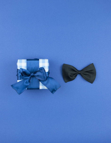 One gift box wrapped in craft paper and tied with bow on dark blue paper background. Concept Father's Day or Birthday background. Top view. International men's day concept. - Photo, Image