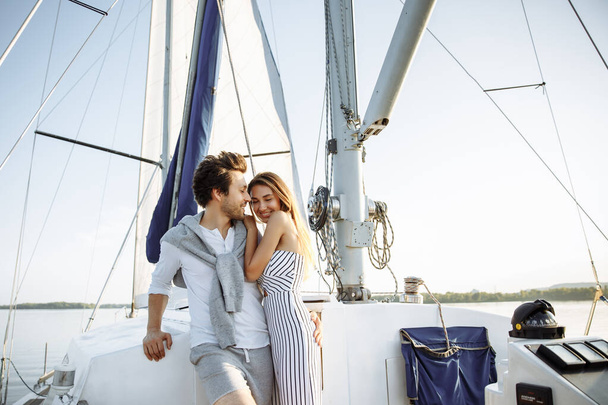 Красивая молодая пара на парусной яхте на закате. Легкая одежда, шорты и брючный костюм. Объятия и смех
 - Фото, изображение