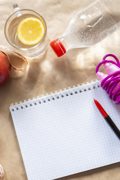 Diet planning. Meal plan - healthy food: Fresh water bottle, skipping rope and an apple with an empty notepad - Photo, Image