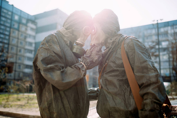 Couple in love hugs in NBC protective suits and gas masks. Concept of a preventive measures and protection for coronavirus COVID 19 pandemic and other global dangers. Backlight. - Photo, Image