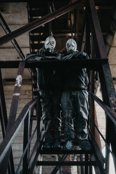 Para zakochanych stoi pod mostem w kombinezonach ochronnych NBC i maskach gazowych. Koncepcja środków zapobiegawczych i ochrona przed pandemią i innymi zagrożeniami globalnymi związanymi z koronawirusem COVID 19. - Zdjęcie, obraz