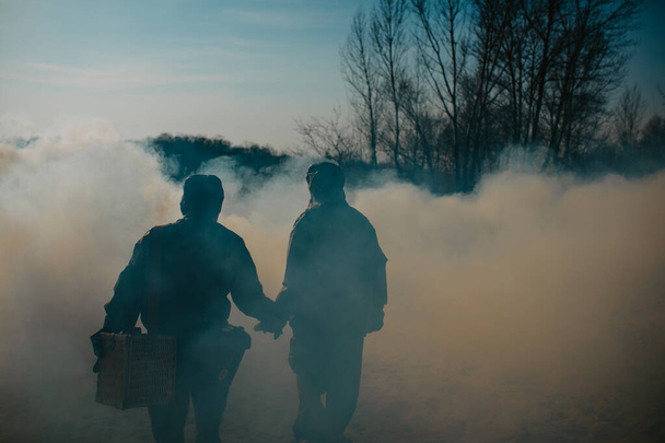 Birbirine aşık bir çift, NBC koruyucu giysileri ve gaz maskeleriyle duman içinde yürüyor. Kıyametin önleyici tedbirleri ve korunması kavramı, küresel çevre kirliliği ve salgın hastalık. - Fotoğraf, Görsel