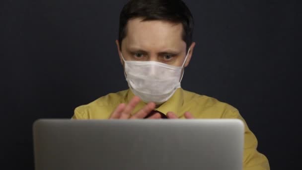 A man in a medical mask sits at a laptop and participates in communication via the Internet. Gestures widely and shows the interlocutor a throat spray. Self-isolation during the coronavirus epidemic. - Πλάνα, βίντεο
