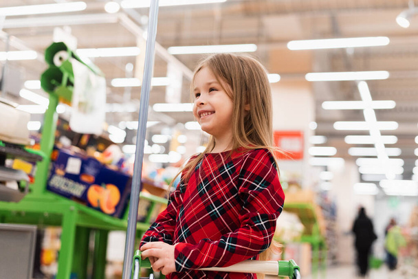 Értékesítés és vásárlás. Kis aranyos lány bevásárlókocsi áll élelmiszerbolt vagy szupermarket élelmiszerbolt. Ázsiai gyerek Vásárlás szupermarketben. - Fotó, kép