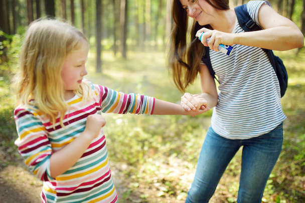 Mother applying insect repellent to her daughter before forest hike beautiful summer day. Protecting children from biting insects at summer. Using bug spray. Active leisure with kids. - Foto, imagen