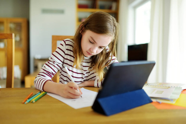Preteen schoolgirl doing her homework with digital tablet at home. Child using gadgets to study. Education and distance learning for kids. Homeschooling during quarantine. Stay at home entertainment. - Foto, Bild