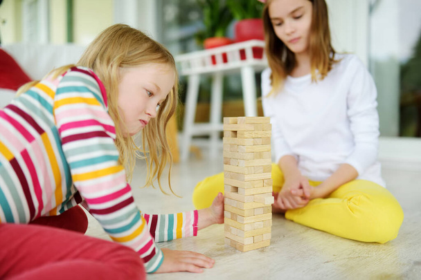 Two cute sisters playing wood blocks tower game at home. Kids practicing their physical and mental skills. Fun board games for family leisure. Stay at home activity for kids. - Fotografie, Obrázek