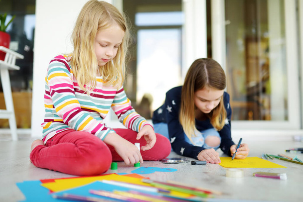 Дві молодші сестри малюють різнокольоровими олівцями вдома. Креативні діти роблять ремесла разом. Освіта та дистанційне навчання для дітей. Вдосконалення під час карантину. Залишайтеся вдома розваги
. - Фото, зображення