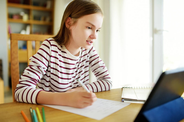 Preteen schoolgirl doing her homework with digital tablet at home. Child using gadgets to study. Education and distance learning for kids. Homeschooling during quarantine. Stay at home entertainment. - Φωτογραφία, εικόνα